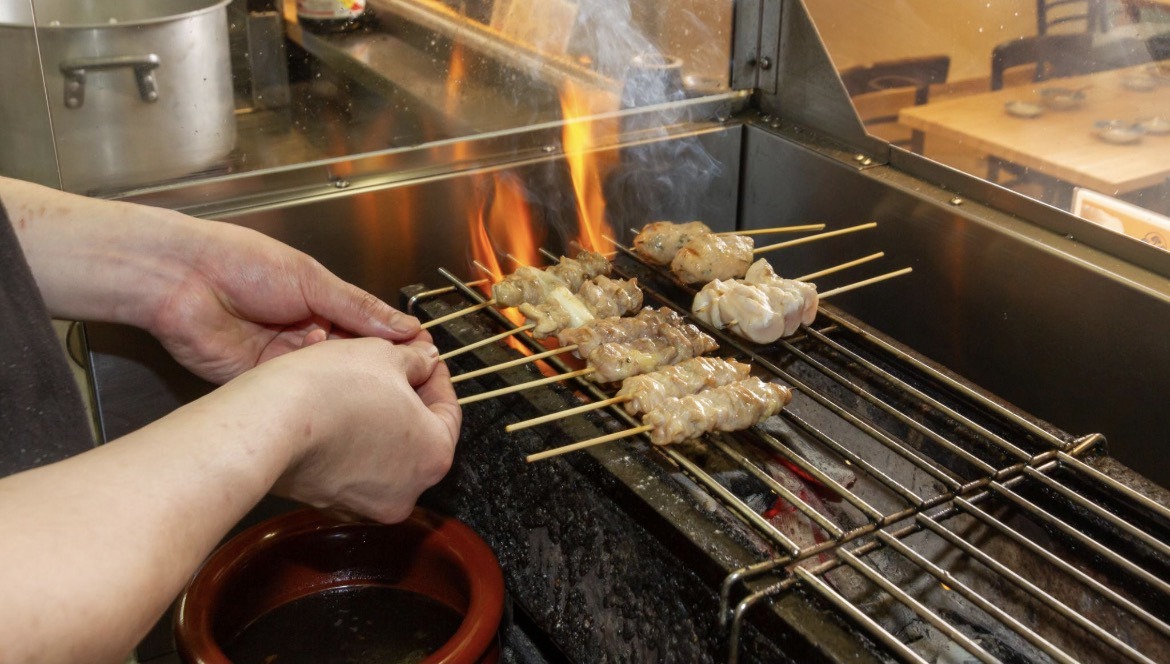 焼鳥店の焼き場で串の焼き加減と提供品質を確認する様子
